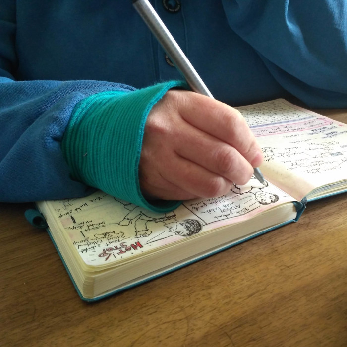 Eine Hand mit Stift schreibt und zeichnet in einem Buch